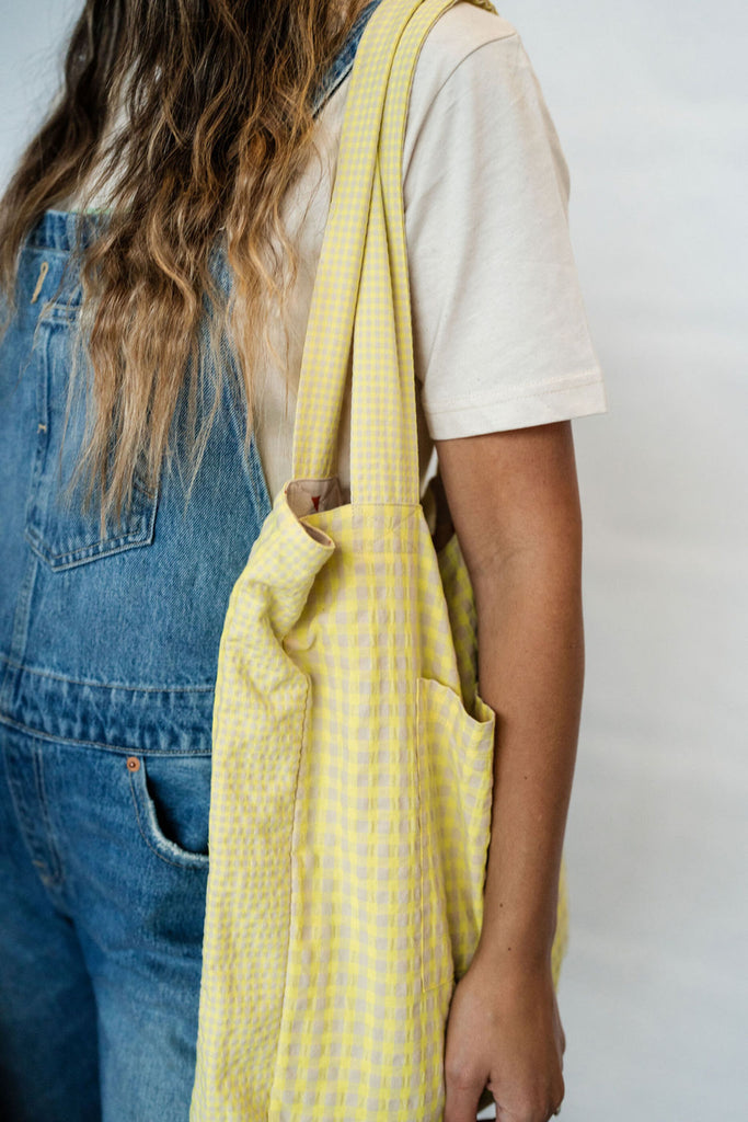 A shot of a person standing with a yellow gingham checked tote bag over their shoulder from Cub & Pudding